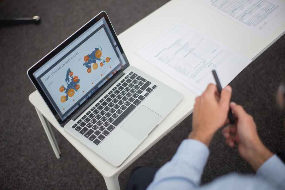 Profesionalac analizira podatkovne infografike na laptopu u uredu, s dokumentima i olovkom